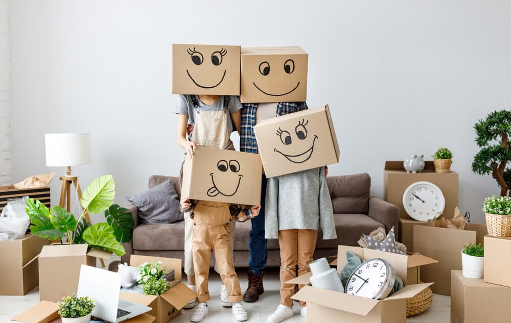 Famille joyeuse avec cartons-têtes souriants au milieu de boîtes de déménagement dans leur nouvelle maison.