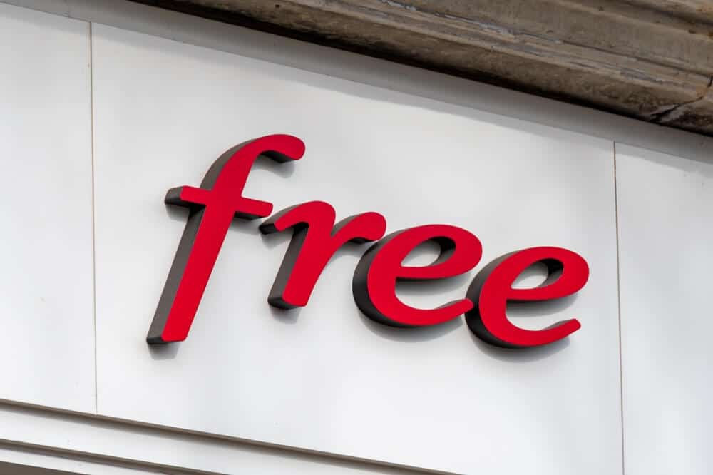 Enseigne rouge et noire 3D du logo "Free" sur une façade blanche. Symbole d'un opérateur télécom français.