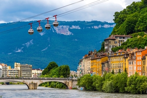 Grenoble : Téléphérique des bulles sur l'Isère, bâtiments colorés, pont en pierre, et montagnes verdoyantes.