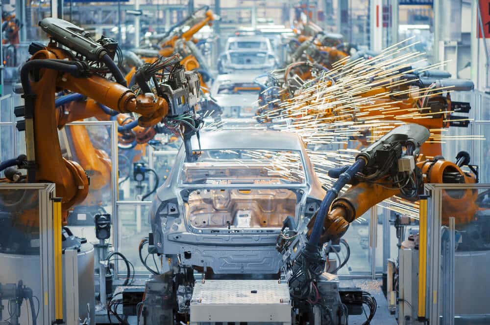 Robots industriels soudant des carrosseries de voiture dans une usine automobile. Des étincelles jaillissent des points de soudure automatisée.
